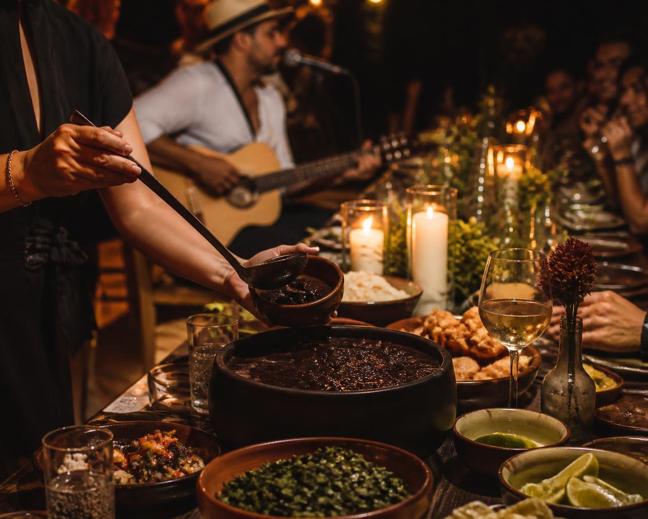 Mesa longa iluminada por velas com feijoada servida e música ao vivo